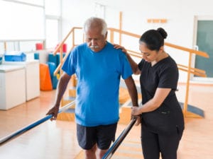 Nurse helping senior student walk in parallel bars