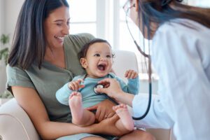 Shot of a baby sitting on her mother's lap while being examined by a Family medicine doctor