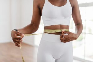 A Black woman measuring her waist with a tape measure as part of her weight loss journey.