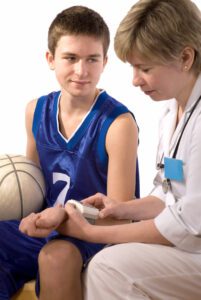 A teenage basketball player is having his arm examined during his sports physical.