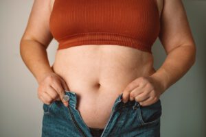 A woman struggling to fit into tight jeans due to being overweight.